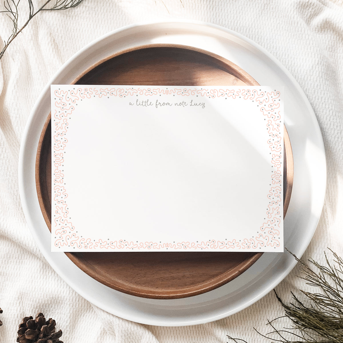 An A6 white stationery card with a blush pink decorative border and gold script text at the top.