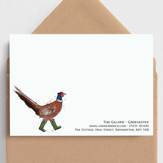 A white stationery card with a whimsical illustration of a pheasant walking in green boots and black printed contact details, shown with a brown kraft envelope on a light gray background.